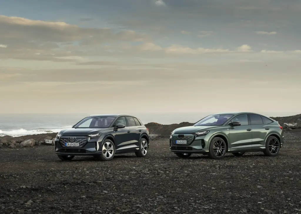 Dwa modele Audi Q4 e-tron – wersja SUV oraz Sportback – zaparkowane obok siebie na skalistym wybrzeżu.