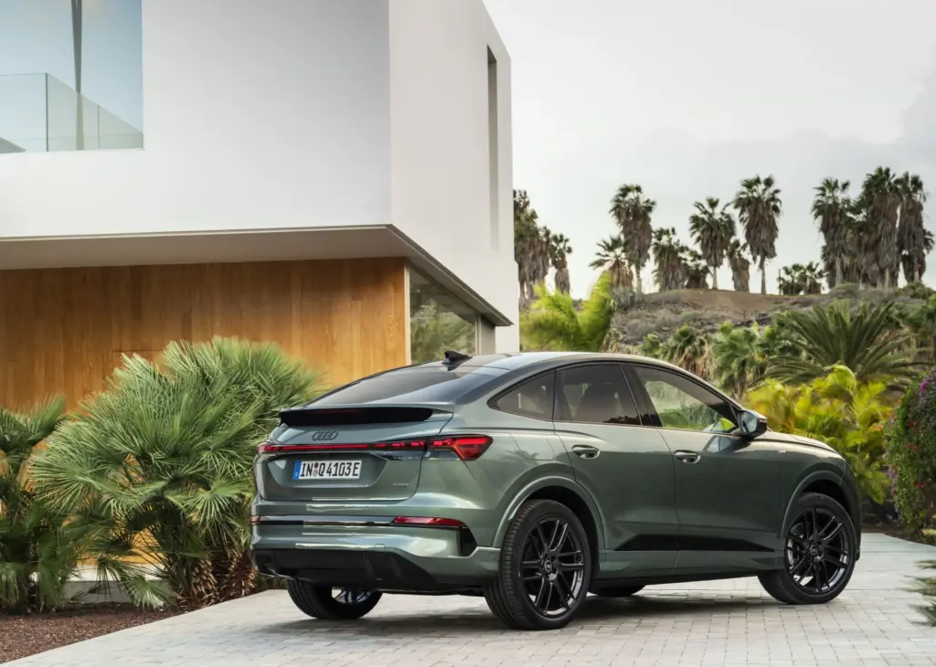 Tylny profil Audi Q4 Sportback e-tron w zielonym kolorze, zaparkowanego przed nowoczesną białą willą.