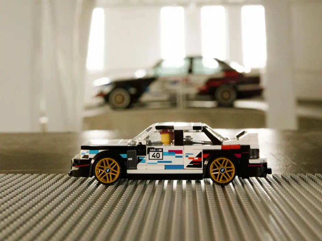 Boczny profil modelu LEGO BMW M3 E30 Speed Champions z prawdziwym BMW M3 E30 w tle.