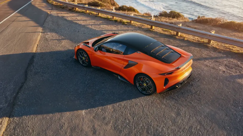 Lotus Emira 420 Sport pomarańczowe coupe na drodze przy wybrzeżu