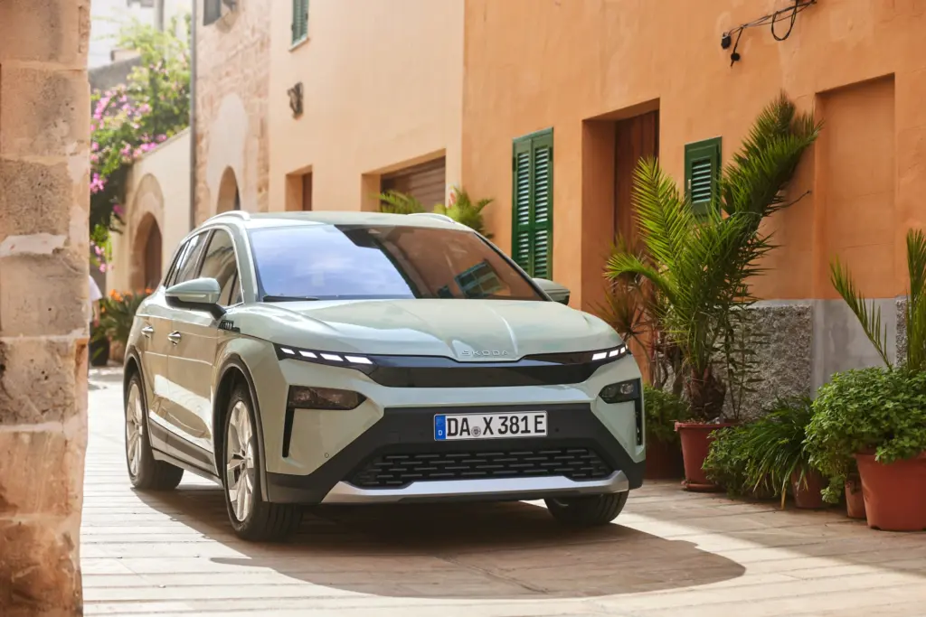 Zielona Skoda Elroq zaparkowana w malowniczej, słonecznej europejskiej uliczce.