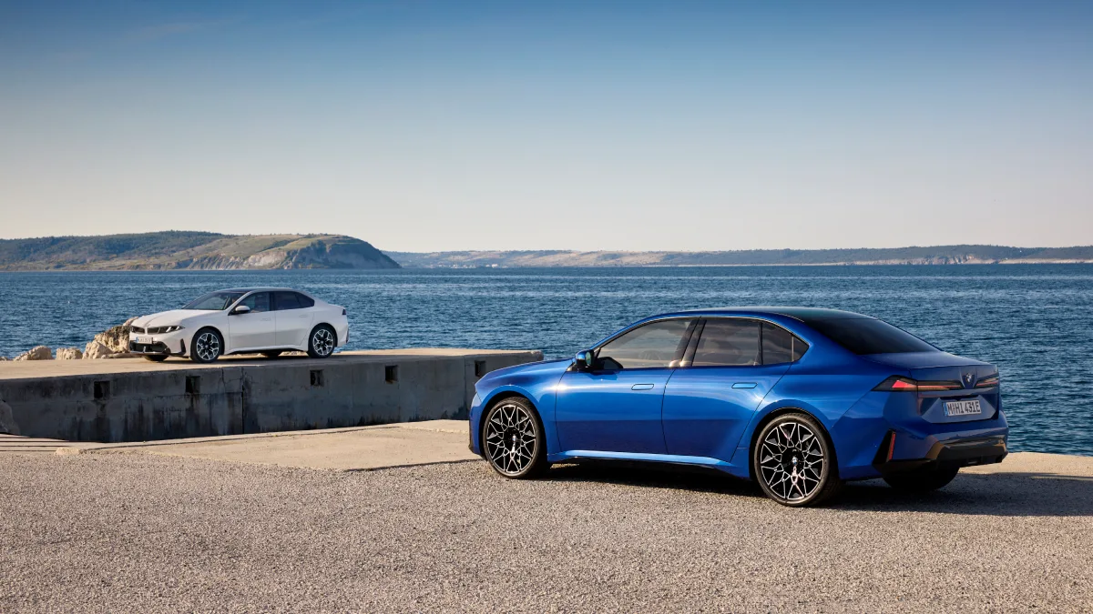 Niebieskie BMW i3 widziane od tyłu i białe BMW serii 3 zaparkowane nad wodą