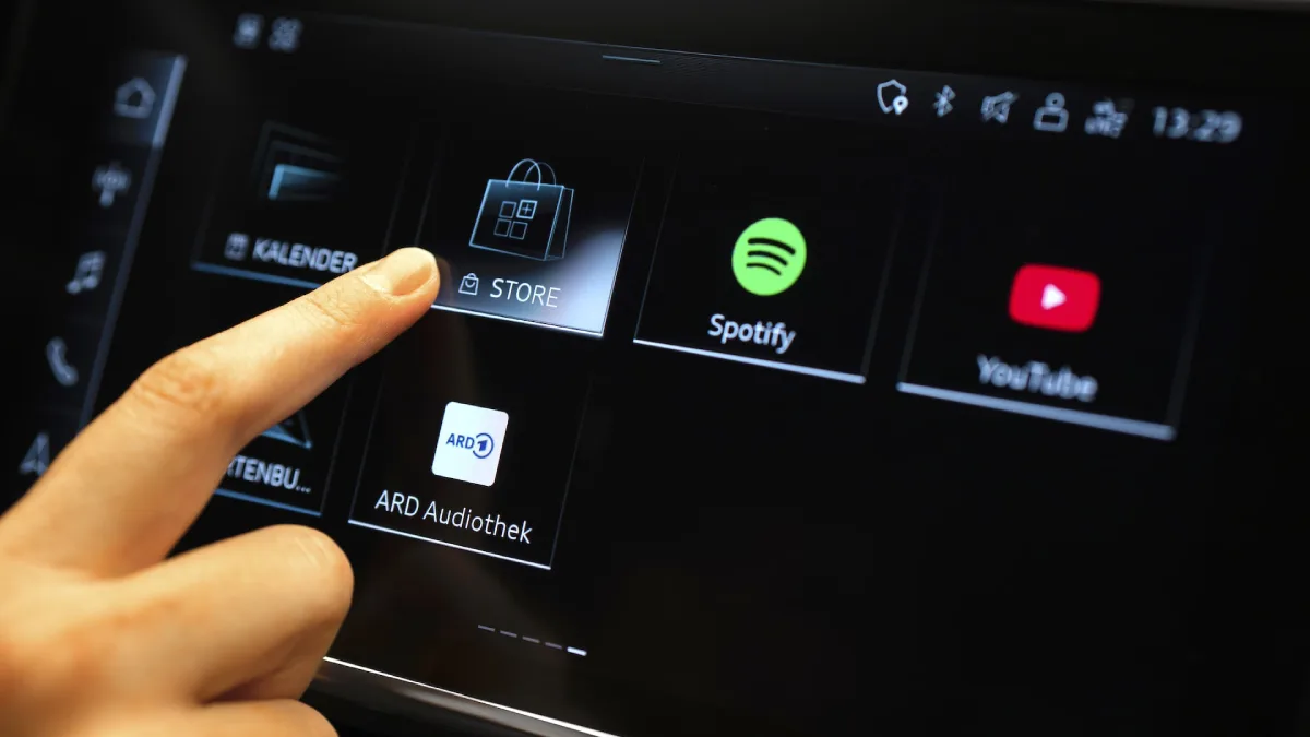 Ekran Audi Application Store w systemie MMI z ikonami Spotify i YouTube oraz dłonią wskazującą sklep z aplikacjami