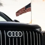 Podświetlone logo Audi na grillu SUV-a i flaga USA w tle, symbolizujące planowaną budowę fabryki Audi w Georgii