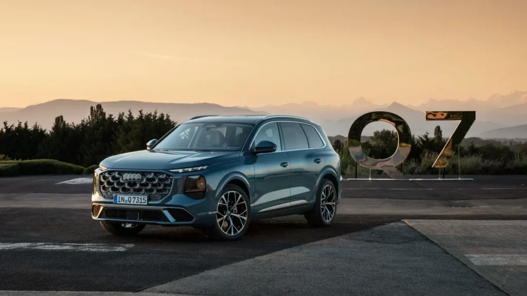 Audi Q7 Euro NCAP 2026, niebieski SUV widziany z przodu i boku na tle górskiego krajobrazu i dużego napisu Q7