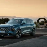 Audi Q7 Euro NCAP 2026, niebieski SUV widziany z przodu i boku na tle górskiego krajobrazu i dużego napisu Q7