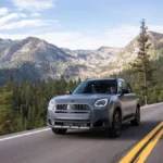 MINI Countryman Untamed Edition podczas jazdy asfaltową drogą na tle gór i lasu