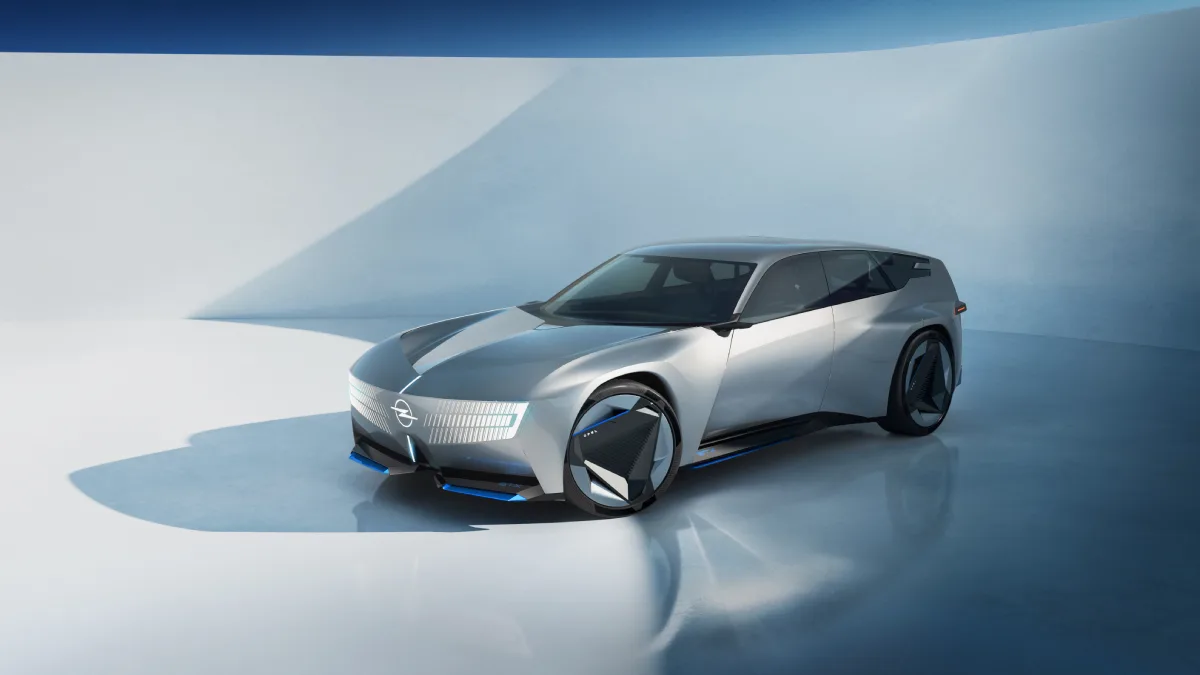 Srebrno-błękitny Opel STX Concept widziany z przodu i boku, z wydłużonym dachem, dużymi kołami i podświetlanym pasem Opel Vizor