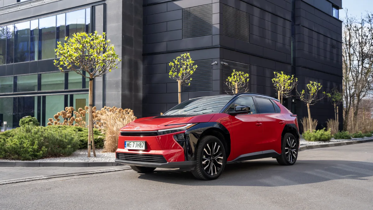 Czerwona elektryczna Toyota bZ4X z czarnymi nadkolami zaparkowana przed nowoczesnym budynkiem