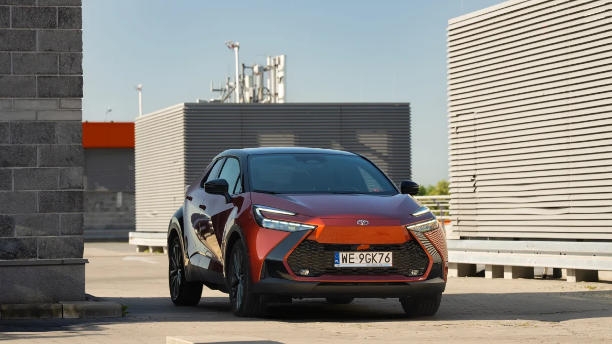 Pomarańczowa Toyota C-HR z czarnym dachem zaparkowana przed nowoczesnym budynkiem